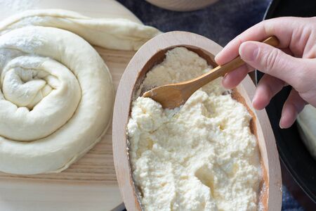 Female hand picking up molten cheese from wooden bowl.Cheese pie visible on the wooden plateの写真素材
