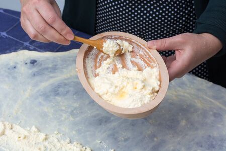 Making of Homemade cheese Pie or other kind of pastry. Female hands putting cheese on phyllo dough on the kitchen tableの写真素材