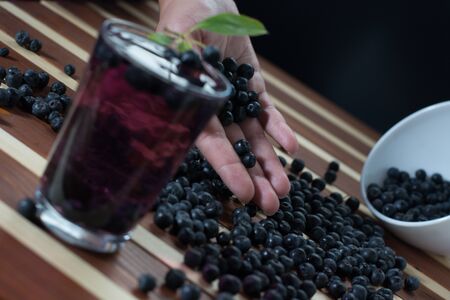 Female hand with aronia and bowl full of aronia spilled on wooden table with glass of aronia juiceの写真素材