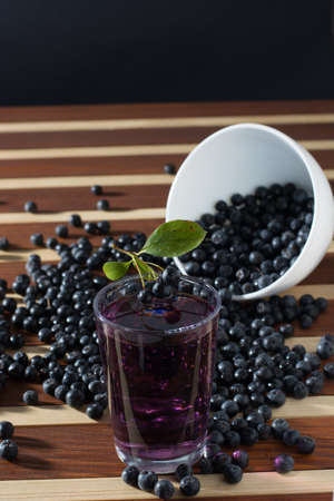 Bowl full of aronia spilled on wooden table with glass of aronia juiceの写真素材