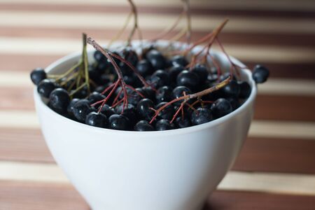 Closeup of wet aronia berries in white simple bowl on wooden tableの写真素材