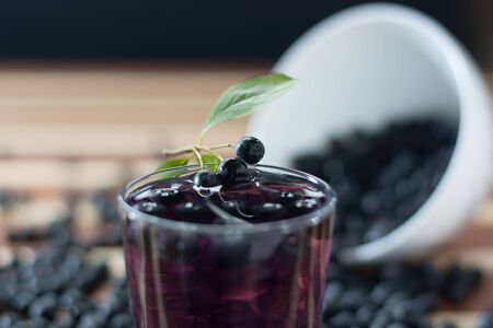 Bowl full of aronia spilled on wooden table with glass of aronia juiceの写真素材