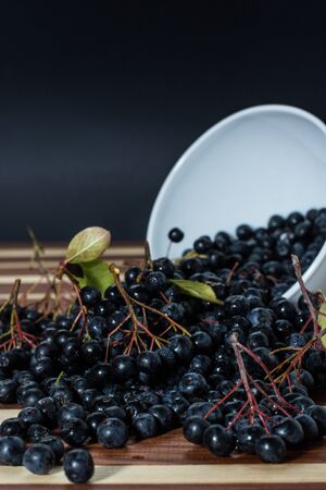 White bowl full with fresh and tasty aronia spilled on wooden tableの写真素材