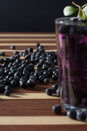 Bowl full of aronia spilled on wooden table with glass of aronia juiceの写真素材