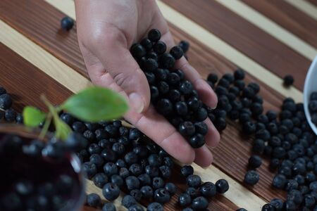 Female hand with aronia and bowl full of aronia spilled on wooden table with glass of aronia juiceの写真素材