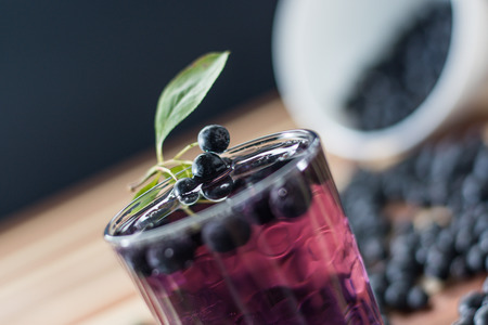 Bowl full of aronia spilled on wooden table with glass of aronia juiceの写真素材