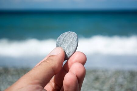Hand with small stone with sea as background