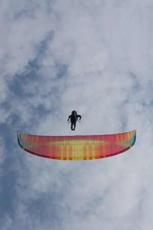 Paraglider flying against the sky with white clouds. Parachute on a clear blue sunny day with sun and clouds.の写真素材