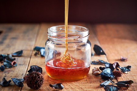 Pouring golden honey in the glass jar on wooden tableの写真素材