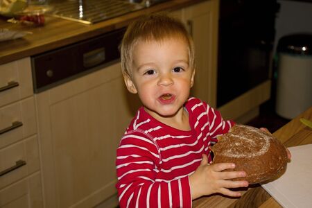 Little blonde boy eat fresh bread.