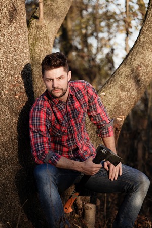 Young, stylish lumberjack felling trees (autumn nature).の写真素材