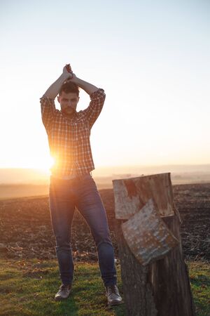 The stylish lumberjack chopping wood at sunset.の写真素材