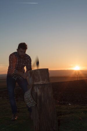 The stylish lumberjack chopping wood at sunset. (Motion blur axe).