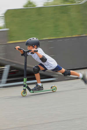 A cute little boy rides a scooter in a skatepark. A young novice athlete spends free time in extreme...