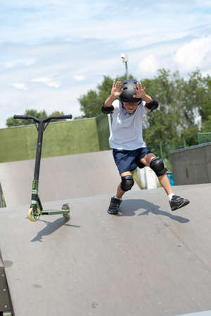 Fall while jumping. A cute little boy rides a scooter in a skatepark. A young novice athlete spends...
