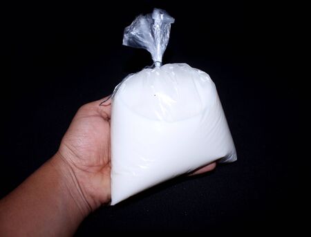 hand holding milk in a plastic polythene packet, dangerous for health on black background - Imageの写真素材