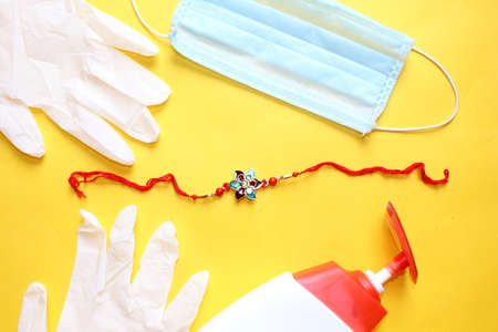 Raksha Bandhan Festival concept in Corona Virus or Covid-19, Rakhi or Wrist Band bracelet with sanitizer, gloves and protective mask for precaution over on yellow background.の写真素材