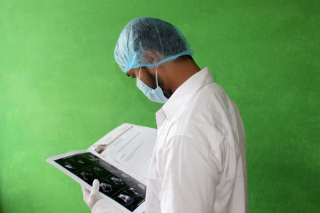 A young doctor in medical uniform with a protective face mask and a gloved reading ultrasound report of patent in covid-19, corona virus.の写真素材