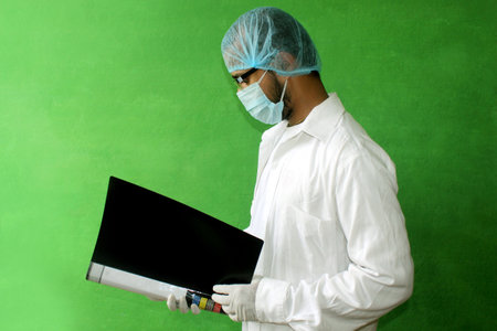 A young doctor in medical uniform with a protective face mask and a gloved reading report file of patent in covid-19, corona virus.の写真素材