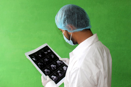 A young doctor in medical uniform with a protective face mask and a gloved reading ultrasound report of patent in covid-19, corona virus.の写真素材