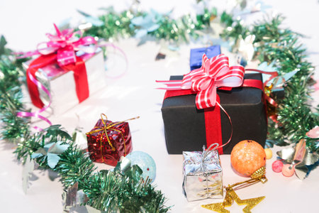 Season's greetings scene. Christmas decorations,gift boxes with red ribbons, Ñhristmas balls, rustic star, holly berries, frosty spruce branches, confetti on white backdrop, selective focus with blurの写真素材