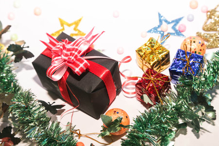 Season's greetings scene. Christmas decorations,gift boxes with red ribbons, Ñhristmas balls, rustic star, holly berries, frosty spruce branches, confetti on white backdrop, selective focus with blurの写真素材