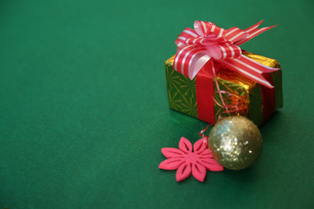 Season's greetings scene.Share your warm wishes with this image idea.view of magnificent giftbox with ribbon, sparkling ornaments, frosty fir, ball, cone on green backdrop, ready for personalized adの写真素材