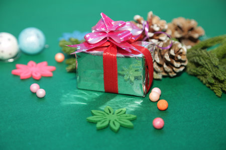 Season's greetings scene.Share your warm wishes with this image idea.view of magnificent gift box with ribbon, snowman, sparkling ornaments, frosty fir, ball, cone on green backdrop, ready for personalized adの写真素材