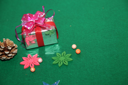 Season's greetings scene.Share your warm wishes with this image idea.view of magnificent gift box with ribbon, sparkling ornaments, frosty fir, ball, cone on green backdrop, ready for personalized adの写真素材