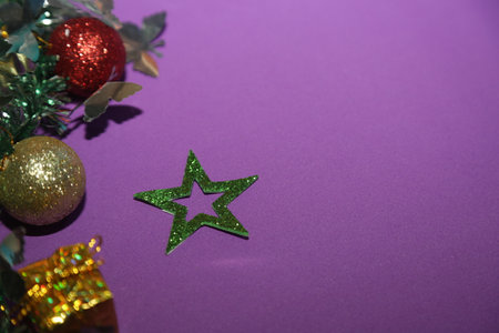 Season's greetings scene. Christmas decorations, balls, rustic star, holly berries, frosty spruce branches, confetti on purple backdrop, perfect for messages or promoの写真素材