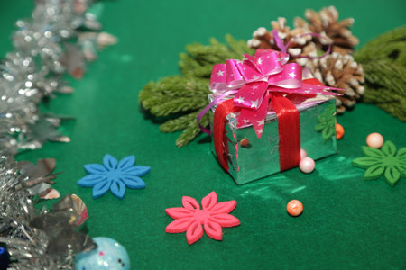 Season's greetings scene.Share your warm wishes with this image idea.view of magnificent gift box with ribbon, sparkling ornaments, frosty fir, ball, cone on green backdrop, ready for personalized adの写真素材