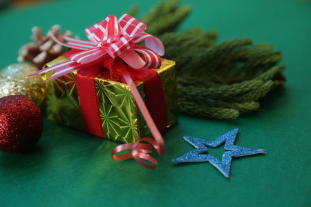 Season's greetings scene.Share your warm wishes with this image idea.view of magnificent giftbox with ribbon, sparkling ornaments, frosty fir, ball, cone on green backdrop, ready for personalized adの写真素材