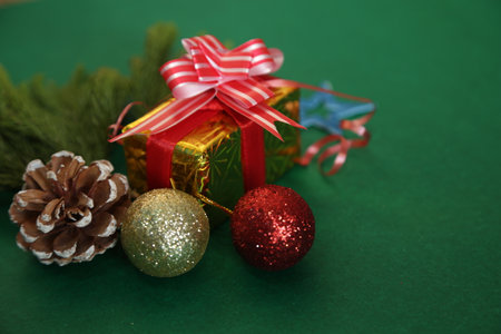 Season's greetings scene.Share your warm wishes with this image idea.view of magnificent giftbox with ribbon, sparkling ornaments, frosty fir, ball, cone on green backdrop, ready for personalized adの写真素材