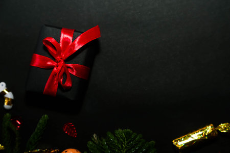 Season's greetings scene.Share your warm wishes with this image idea.view of magnificent gift box with ribbon, sparkling ornaments, frosty fir, ball, cone on black backdrop, with space for your text.の写真素材