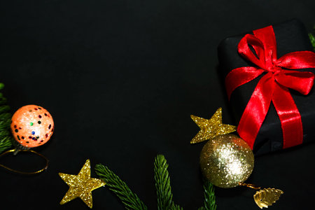 Season's greetings scene.Share your warm wishes with this image idea.view of magnificent gift box with ribbon, sparkling ornaments, frosty fir, ball, cone on black backdrop, with space for your text.の写真素材