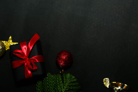 Season's greetings scene.Share your warm wishes with this image idea.view of magnificent gift box with ribbon, sparkling ornaments, frosty fir, ball, cone on black backdrop, with space for your text.の写真素材