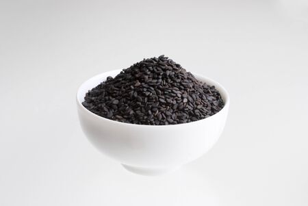 black sesame seeds in porcelain bowl on white backgroundの写真素材
