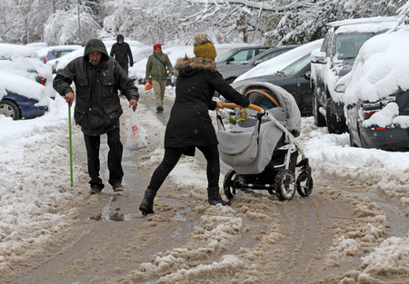 People are walking hard on a snowy icy road after a heavy snowfall in the city of Sofia, Bulgaria on Nov 28,2017, person with cane on an icy pathway, Woman push baby stroller through the dirty snowのeditorial素材