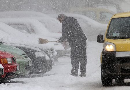 Winter. A man with a broom and shovel cleans car from snow on the street after big snowstormのeditorial素材