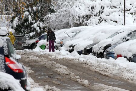 Winter. Snowfall. A man with a broom and shovel cleans car from snow on the street after big snowstorm . Icy windowsの写真素材