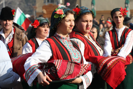 Folklore ensemble with traditional costumes dance horo with ritual bread (loaf) during the international festival  of masquerade games Surva in Pernik, Bulgaria  Jan27,2018. Girls with traditional nosiaのeditorial素材