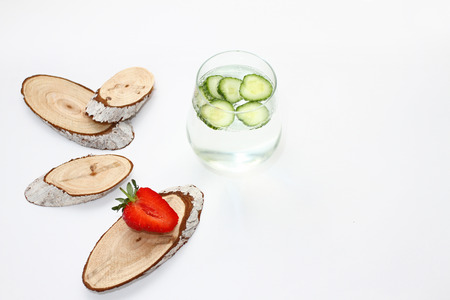 Detox flavored water with cucumber on white background with red strawberry and wood decoration. Healthy food concept.  Refreshing summer homemade cocktail. Copy space. No sharpen. Anti stress drink.の写真素材