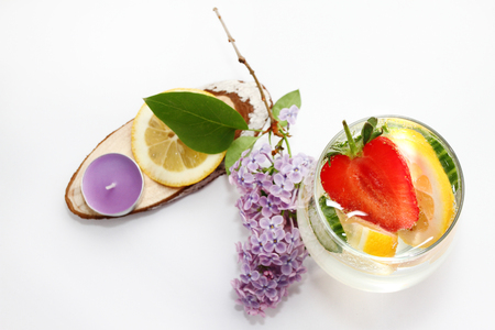 Detox flavored water with lemon, cucumber and  strawberry on white background with lilac and wood decoration. Healthy food concept.  Refreshing summer homemade cocktail. Copy space. No sharpen.の写真素材