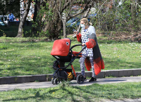Woman with face mask for protection from coronavirus push a stroller in the street in Sofia,...