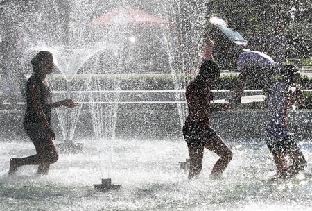 Unrecognizable children are playing in a fountain under the water in the summer heat.の写真素材