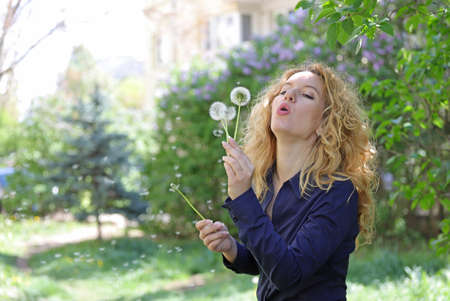 Blond young woman blows a dandelion in natureの写真素材