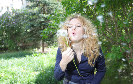 Blond young woman blows a dandelion in natureの写真素材