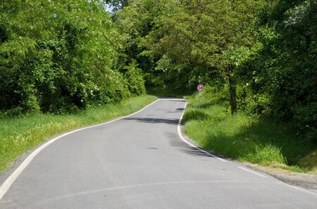 Road in Italy winds through the forest and the road sign.の写真素材