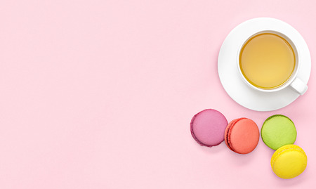 Flat lay photo of office desk with   tea mug, macaroons on pink backgroundの写真素材