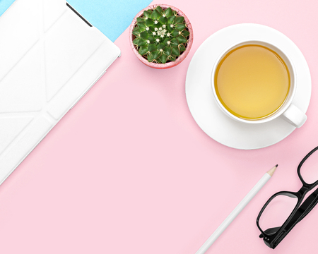 Flat lay photo of office desk with tablet computer, tea mug, pencil, cactus, glasses, on pink and blue backgroundの写真素材